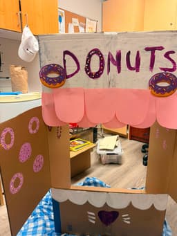 A hand-painted cardboard donut stand built by volunteers, with a pink scalloped awning